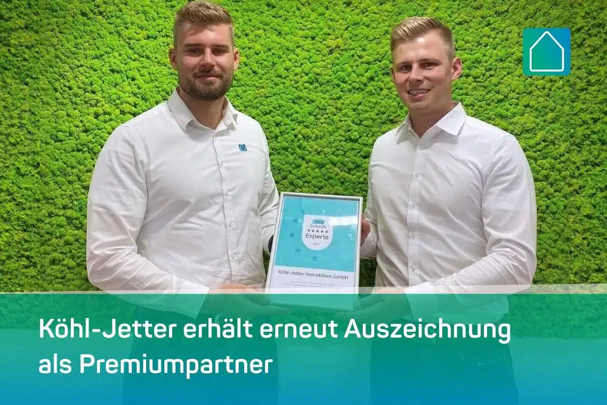Zwei Männer in weißen Hemden stehen vor einer grünen, mit Pflanzen bedeckten Wand. Sie halten eine Urkunde in den Händen. Der überlagerte Text in Deutsch lautet: Köhl-Jetter erhält erneut Auszeichnung als Premiumpartner.